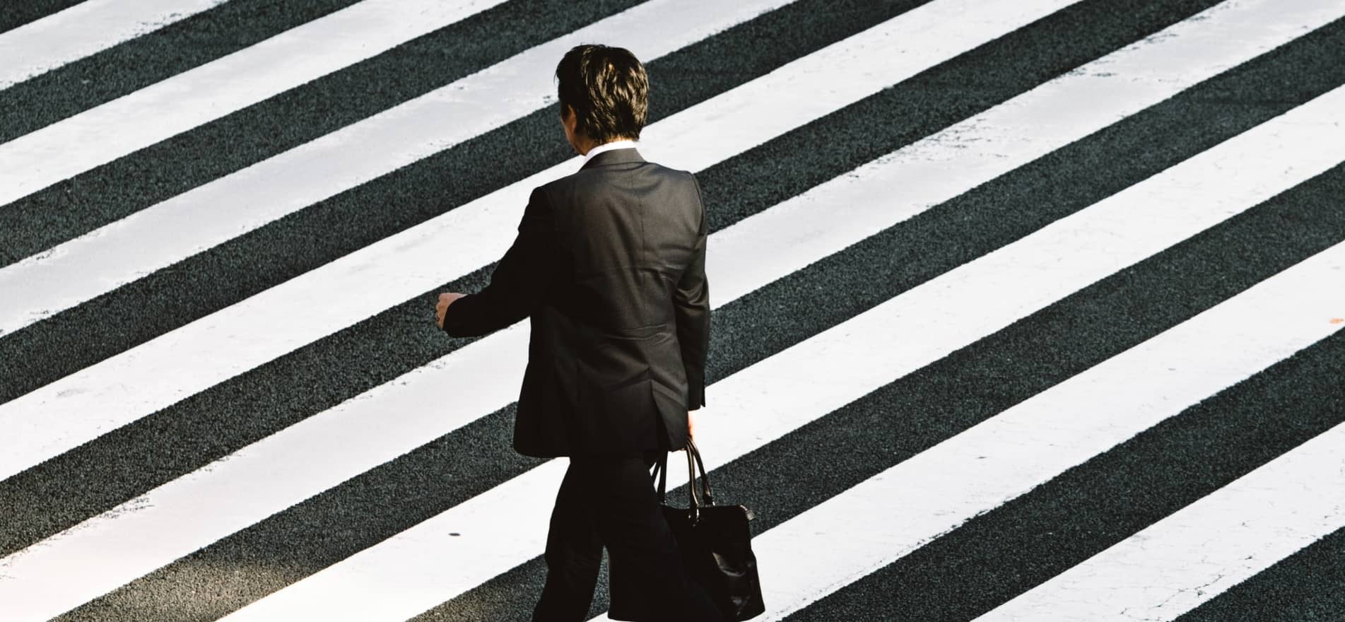 photographie d'un homme en costard noir qui marche sur un passage piéton